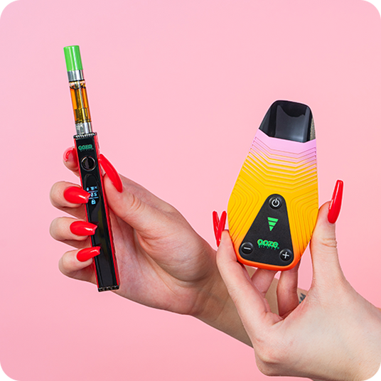 ooze quad 2 and ooze brink dry herb vaporizer held in hands with red fingernail polish over a light pink background